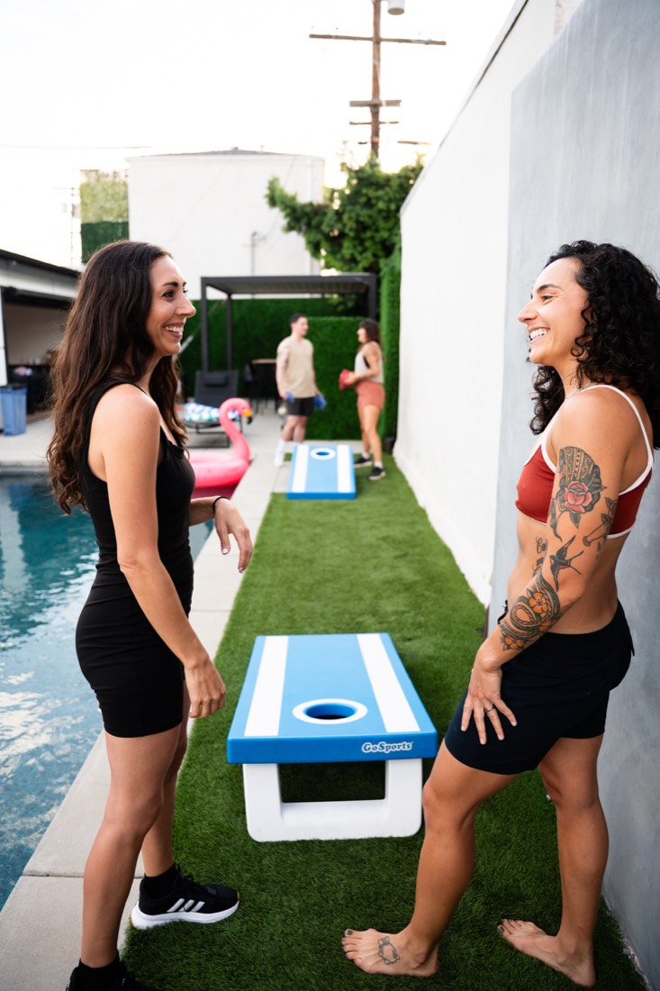 Two women playing cornhole in a backyard